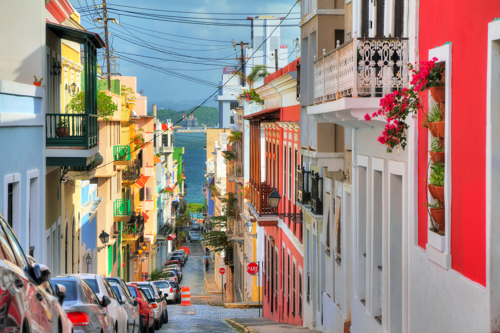 gorgeous view down a colorful street in puerto rico with balconies filled with flowers. view overlooks water